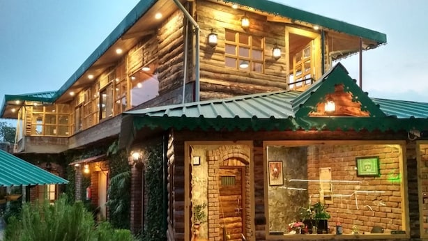 A log cabin-style building with multiple windows and a balcony, surrounded by greenery. - Jharipani Castle (Dehradun)