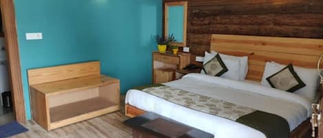 A bedroom with a wooden headboard, a bed with white bedding, a wooden bench, a nightstand with a mirror, and a wall-mounted light fixture.