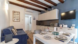 Un espacio de estar moderno con sofá, comedor, área de cocina y televisor montado en la pared.