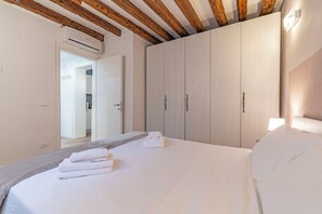 Ein Schlafzimmer mit einem großen Bett, Holzbalken an der Decke, einem Kleiderschrank und einer Klimaanlage.