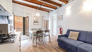 Una cocina moderna con estufa a gas, mesa de comedor con sillas, un sofá azul y techo de madera.