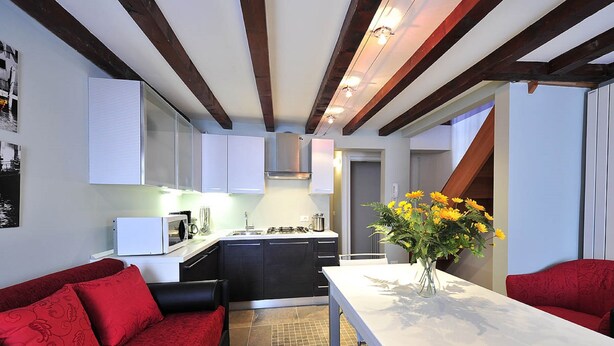A compact kitchen with modern appliances, a dining area with a white table, and a red sofa. - Palace La Vida Apartments by Wonderful Italy (Venice)
