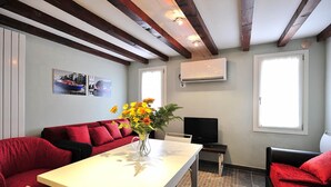 A room with a white table, red sofas, a TV, and a vase with flowers. - Palace La Vida Apartments by Wonderful Italy (Venice)