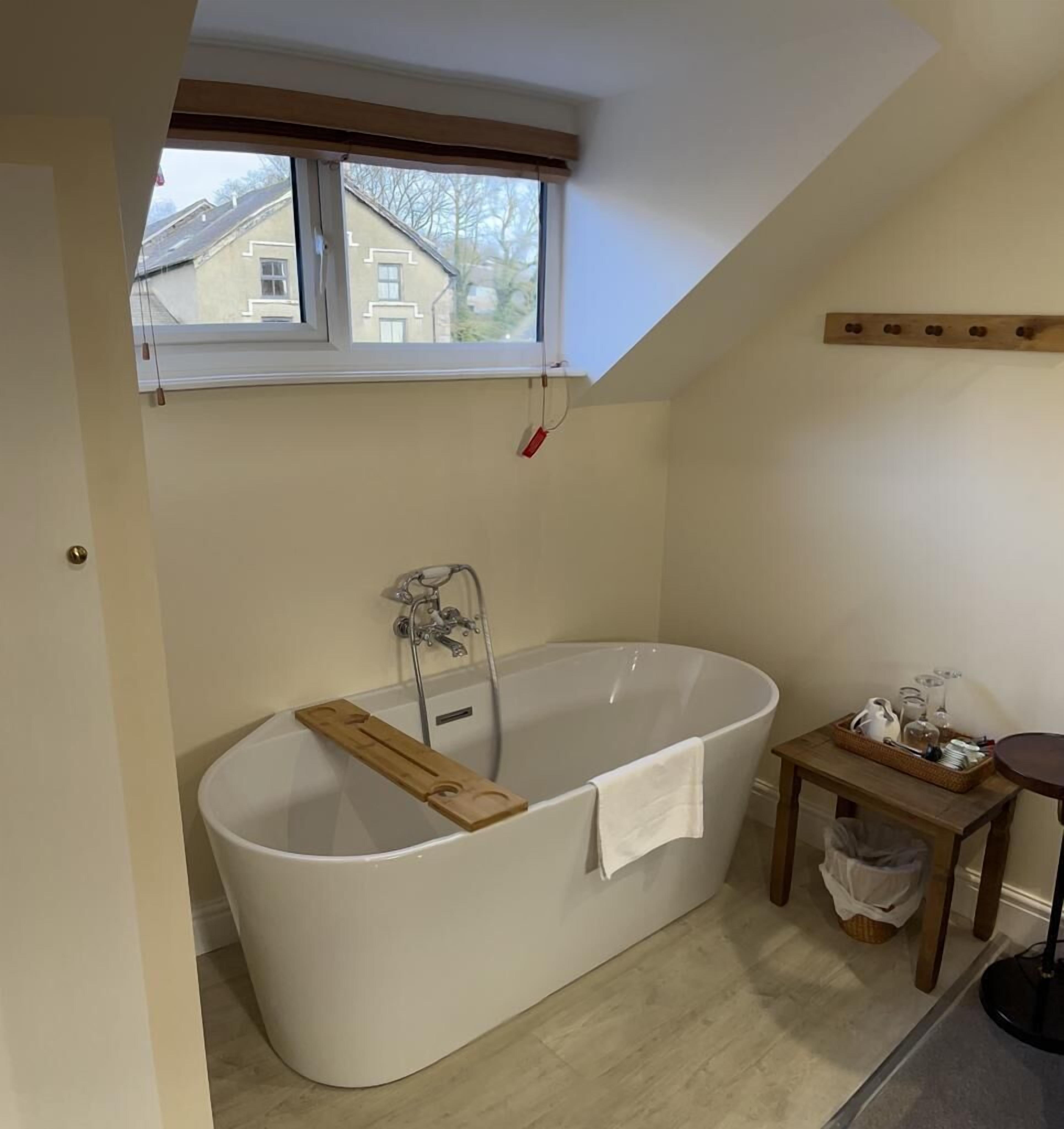 Un bagno con una vasca da bagno indipendente, una finestra, un piccolo tavolino con bicchieri e un porta asciugamani.