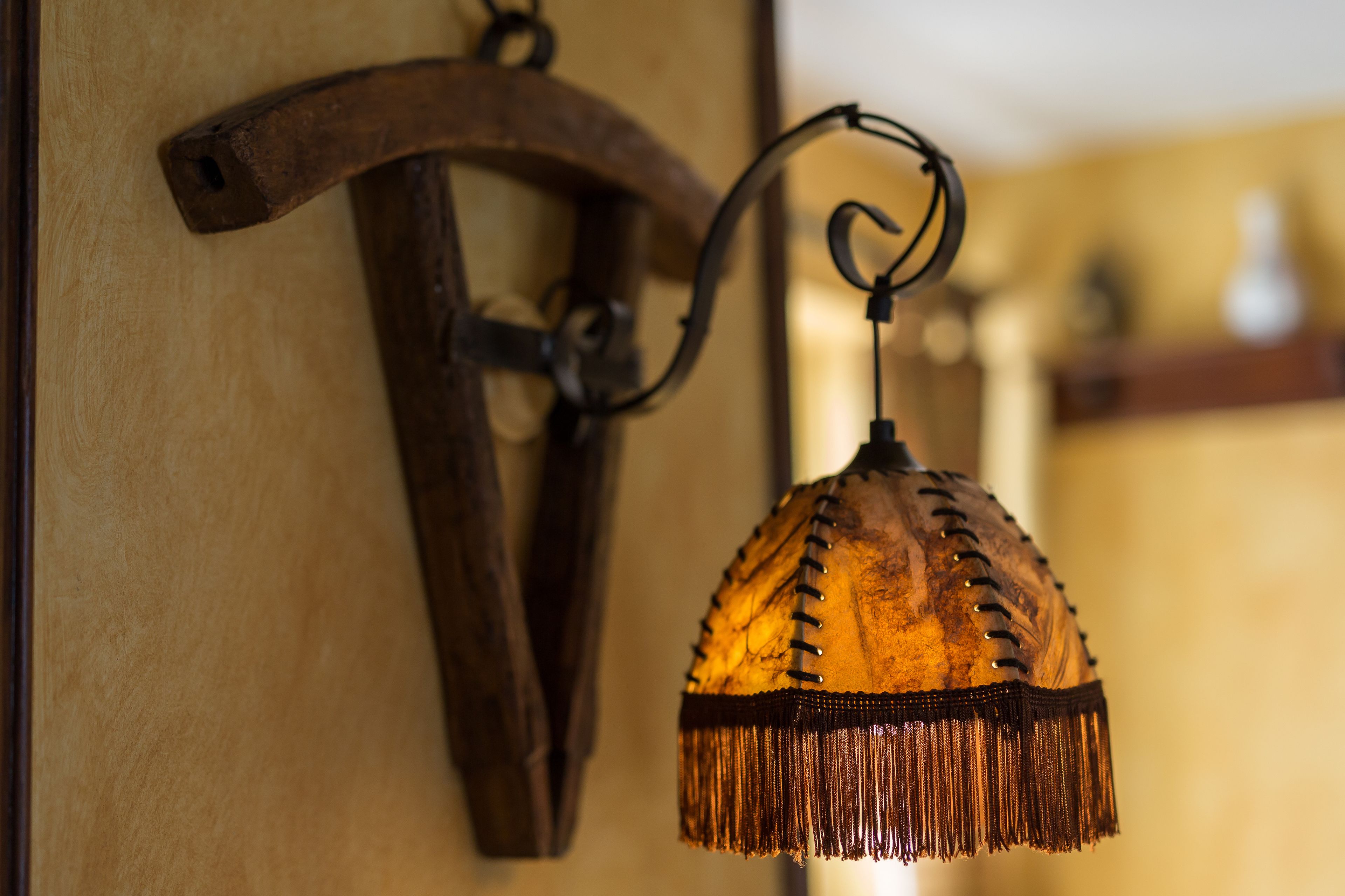 Una lámpara de pared con diseño rústico, que incluye un brazo de madera y un paralume colgante con flecos.