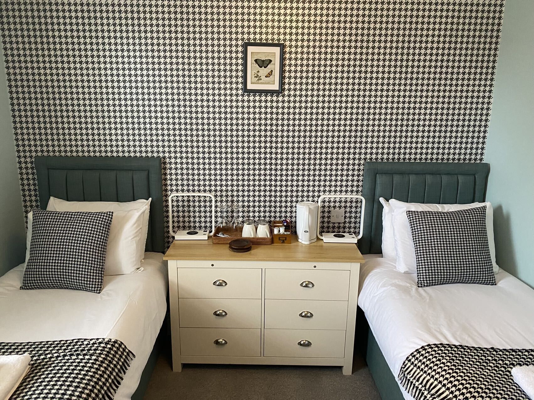 A hotel room with two beds, a nightstand, and a houndstooth-patterned wallpaper.