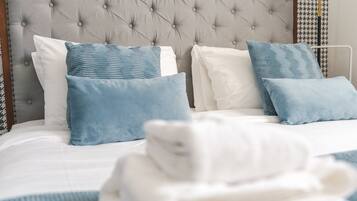 A neatly made bed with a tufted headboard, white and blue pillows, and a folded white towel.