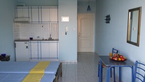 Ein gemütlicher Raum mit einem Bett, einer kleinen Küche mit weißen Schränken, einem Esstisch mit Stühlen und einer Obstschale auf dem Tisch.