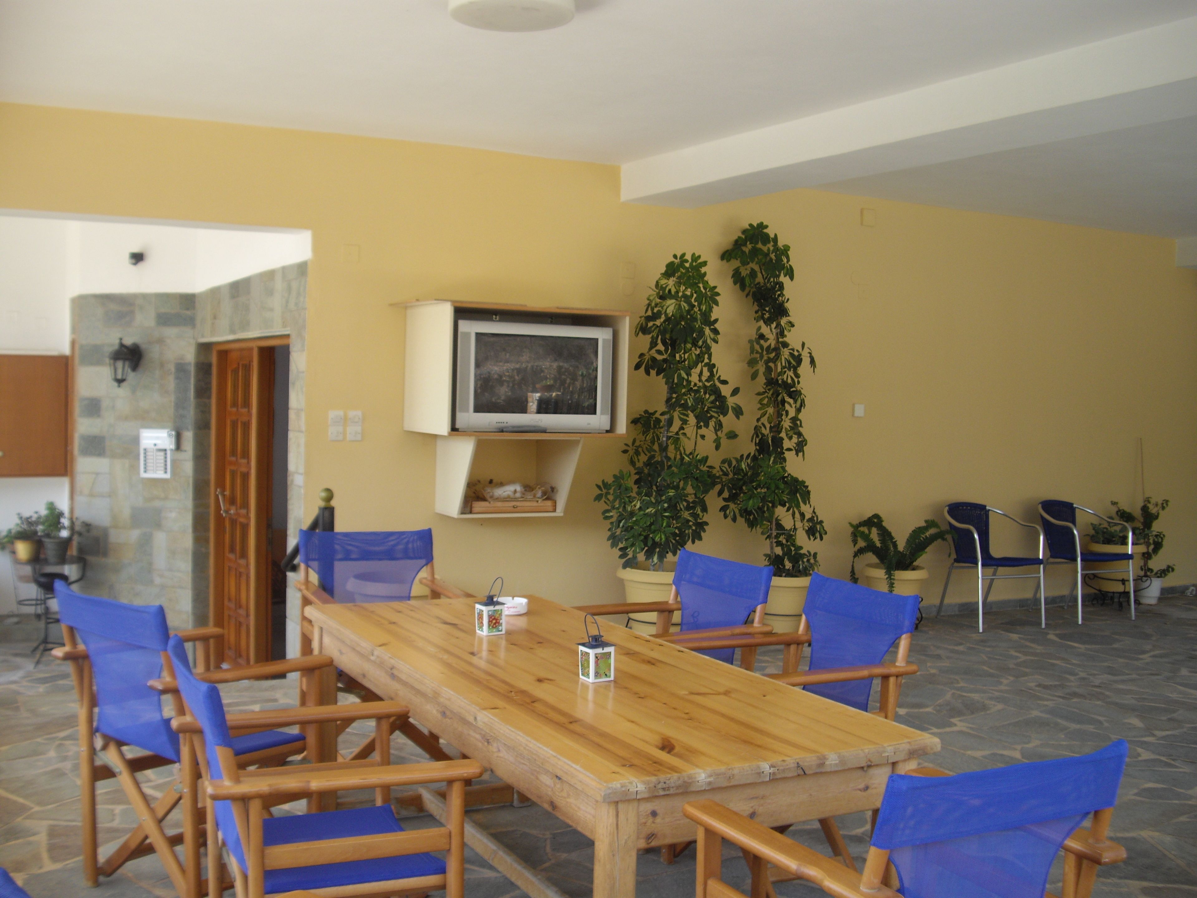Ein Essbereich mit einem Holztisch, blauen Stühlen, einem an der Wand befestigten Fernseher und Blumentöpfen.