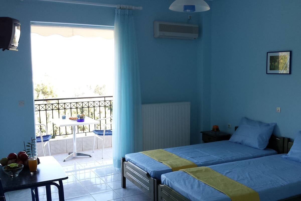 A room with two beds, a table with breakfast items, a balcony with a table and chairs, and a radiator.