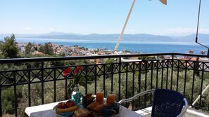 Un balcón con una mesa preparada para el desayuno, con vistas a un pueblo costero y al mar.
