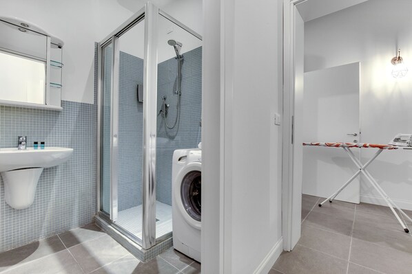 Un baño moderno con ducha de vidrio, lavadora y lavabo con espejo.