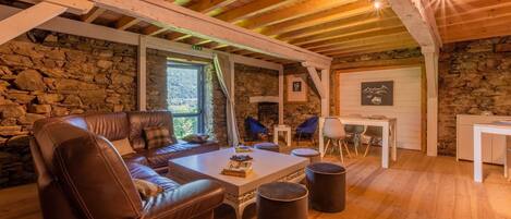 A cozy room with a stone wall, wooden ceiling beams, a leather sofa, a coffee table, and a stone fireplace.