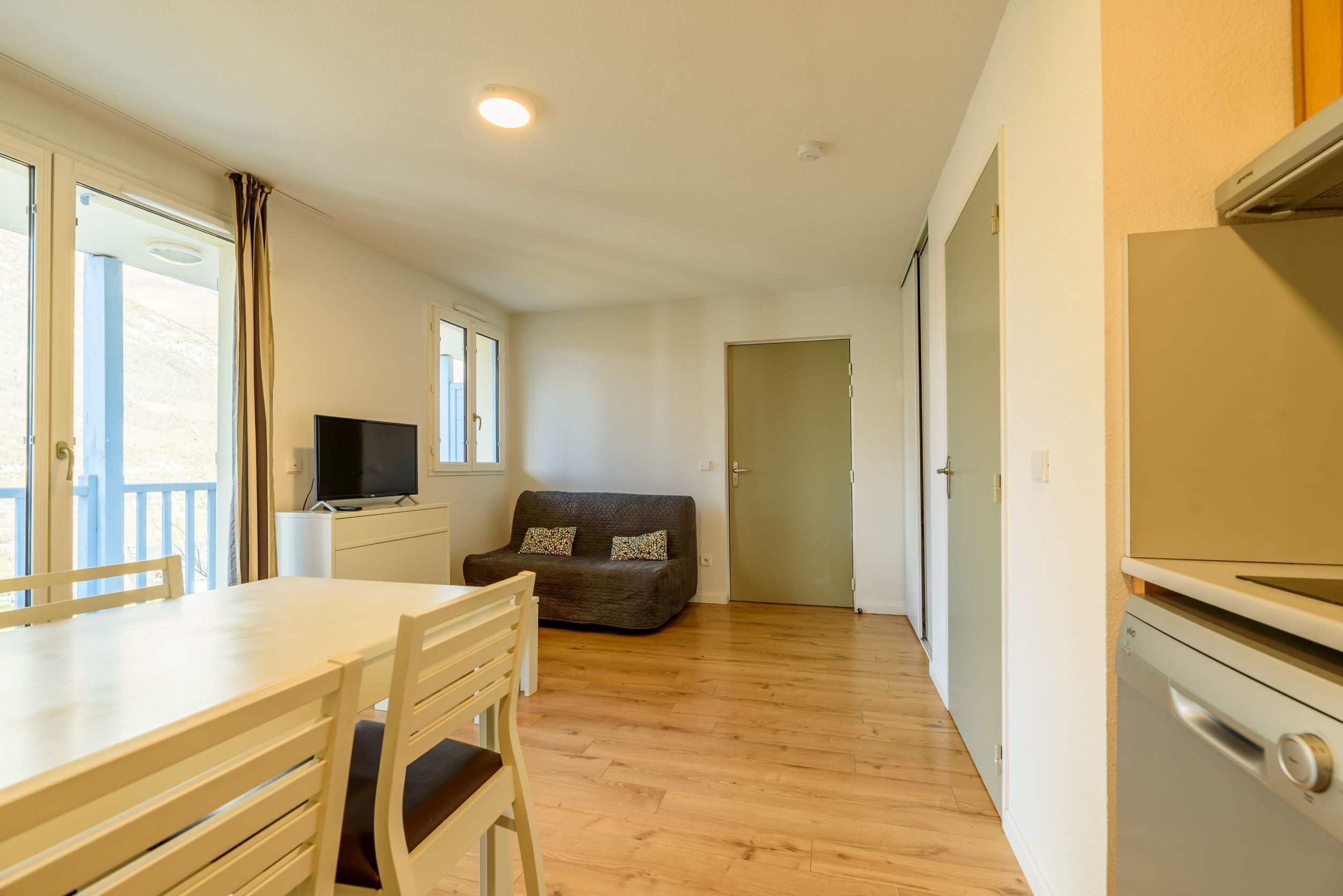 Un espacio habitable compacto con comedor, un sofá, un televisor y una zona de cocina con refrigerador.