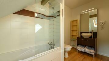 Un baño moderno con ducha envuelta en vidrio, inodoro blanco y tocador de madera con espejo.