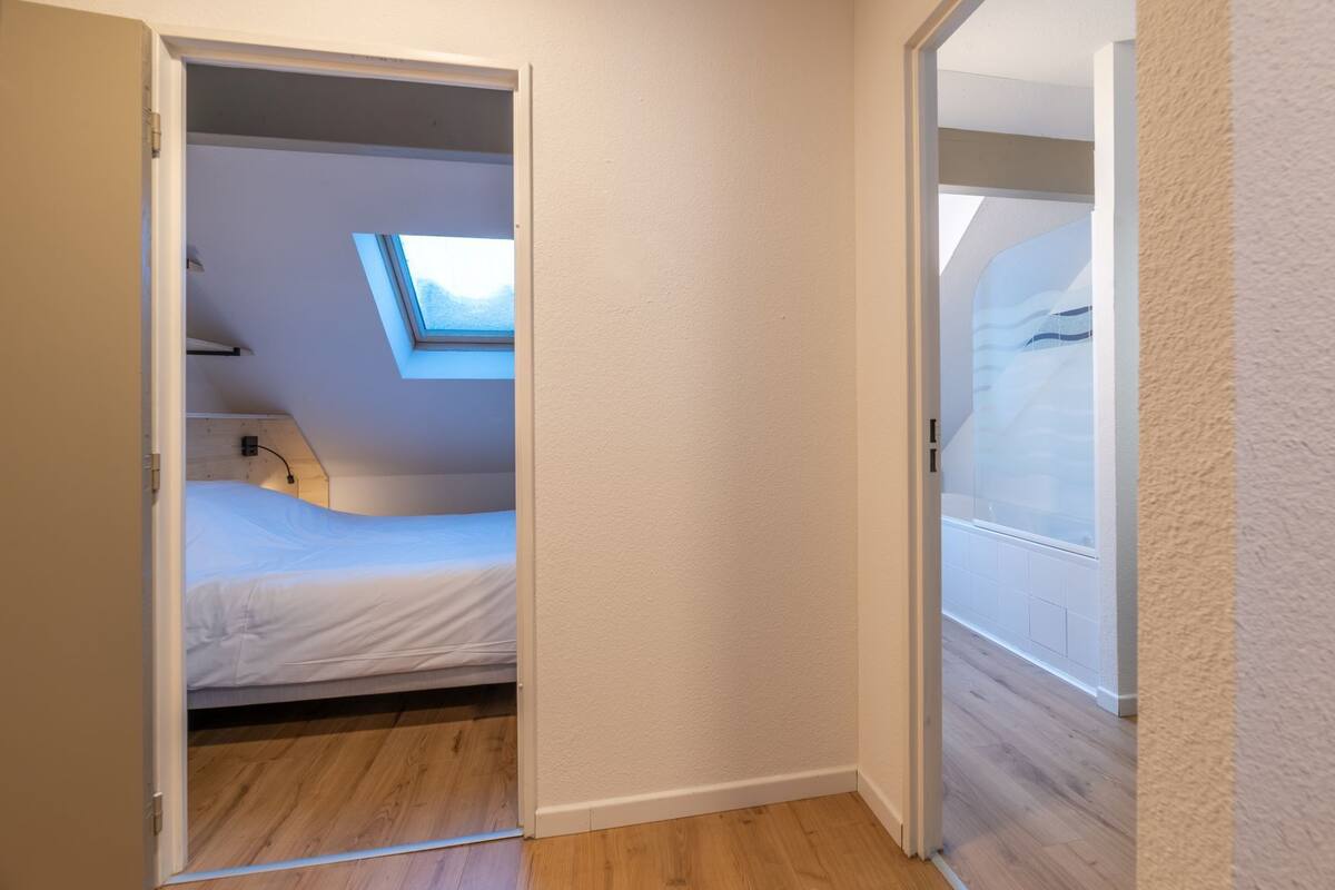 A bedroom with a skylight, wooden flooring, and a white bed.