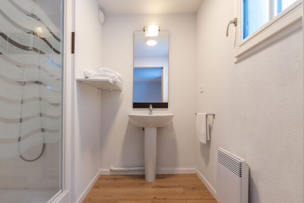 A small, clean bathroom with a white sink, a mirror, a towel rack, and a window.