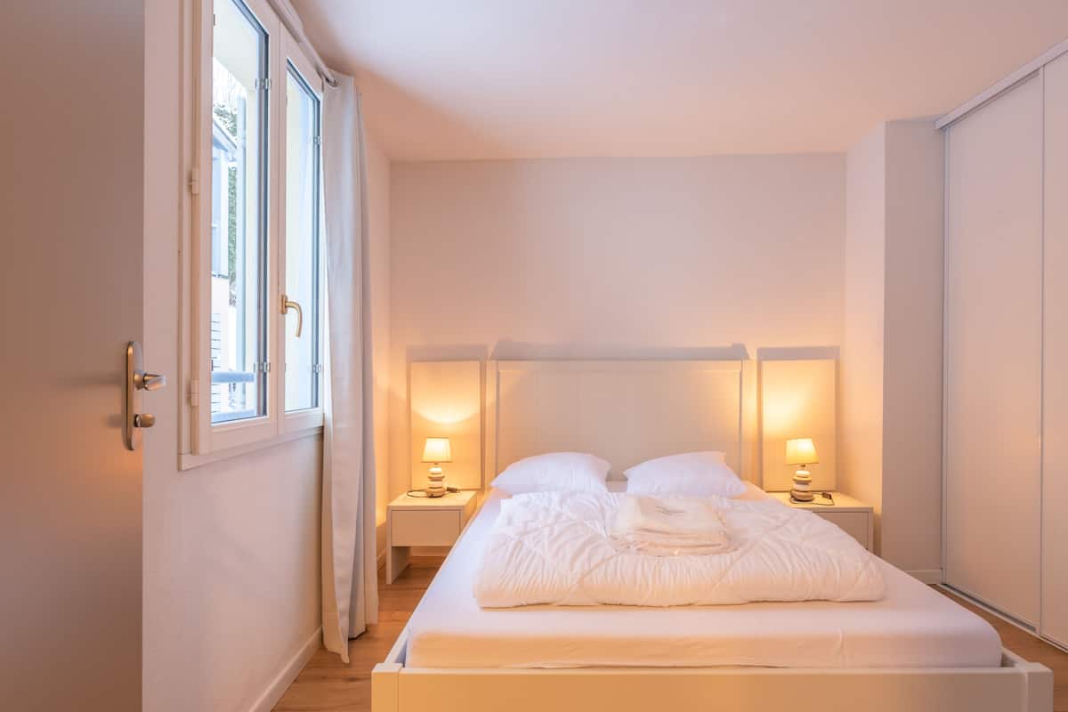 A bedroom with a bed, bedside lamps, and a window.