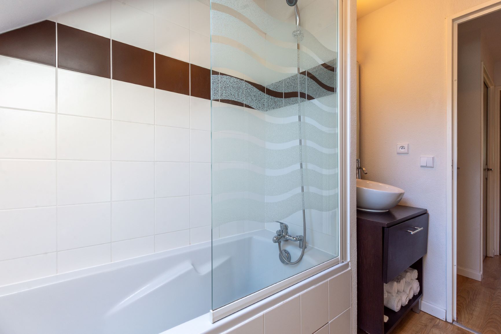 A modern bathroom with a glass-enclosed shower, white tiles, a dark wooden cabinet, and a white sink.