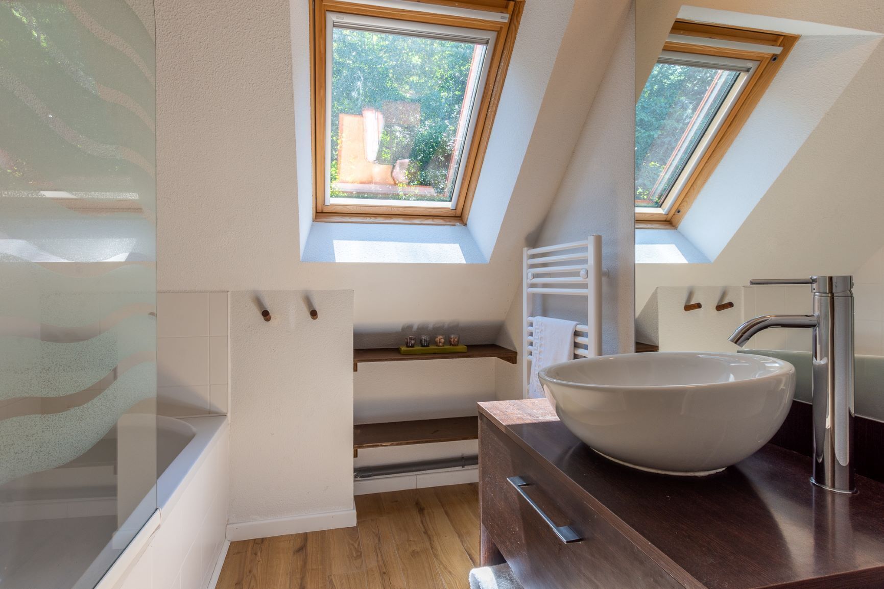 A modern bathroom with skylights, a large vessel sink, and a wooden vanity.