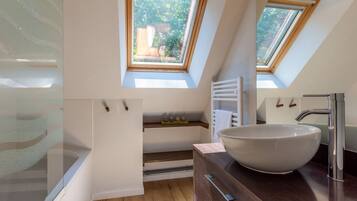 A modern bathroom with skylights, a large vessel sink, and a wooden vanity.