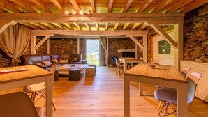 A cozy room with a stone wall, wooden ceiling beams, a leather sofa, a wooden table, and a fireplace. - Résidence Les Balcons de l'Yse (Luz-Saint-Sauveur)