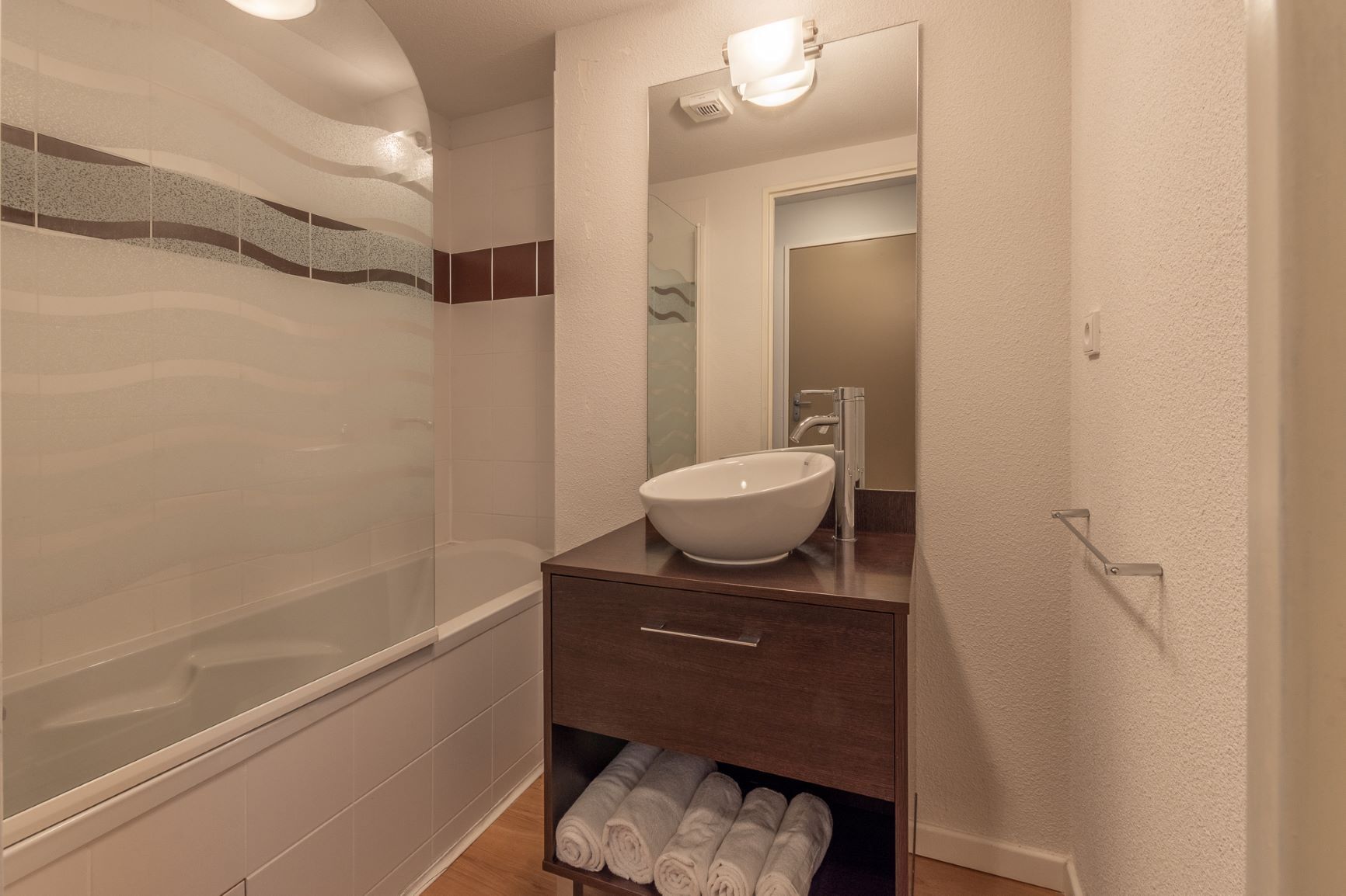 A modern bathroom with a glass-enclosed shower, a white vessel sink, and a wooden vanity with a mirror.
