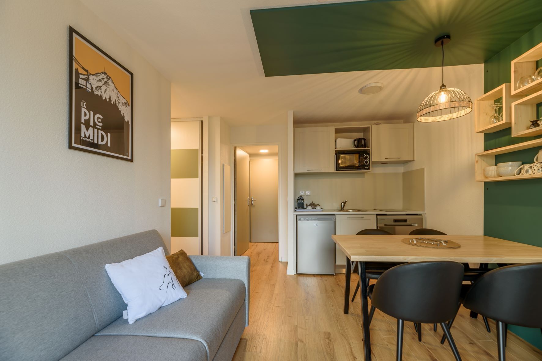 A compact living space with a sofa, a dining table with chairs, a kitchenette, and a ceiling light fixture.