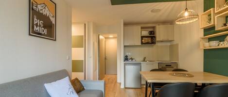 A compact living space with a sofa, a dining table with chairs, a kitchenette, and a ceiling light fixture.