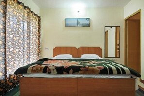 A bedroom with a wooden bed, floral bedding, a mirror, and a painting on the wall. - Janardan Resort Pangot (Kosiyakutoli)
