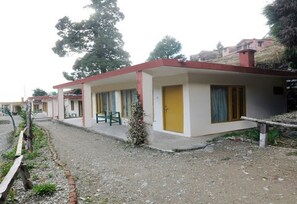 A row of single-story buildings with a simple, functional design, featuring a gravel pathway and minimal landscaping. - Janardan Resort Pangot (Kosiyakutoli)