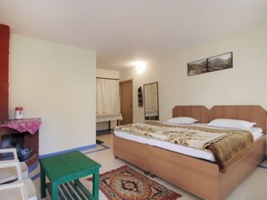 A bedroom with a bed, a green table, a patterned rug, and a painting on the wall. - Janardan Resort Pangot (Kosiyakutoli)