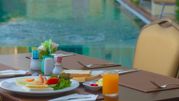 Una mesa de comedor con alimentos para el desayuno, un vaso de zumo de naranja y vistas a una piscina.