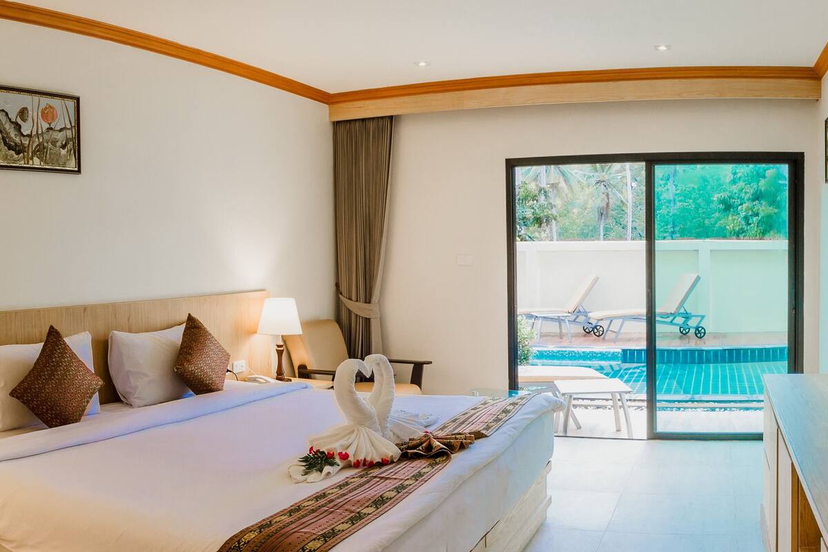 Une chambre d’hôtel comprenant un lit, une télévision, un bureau, une chaise, une fenêtre donnant sur une piscine et un espace verdoyant, ainsi qu’un tableau accroché au mur.
