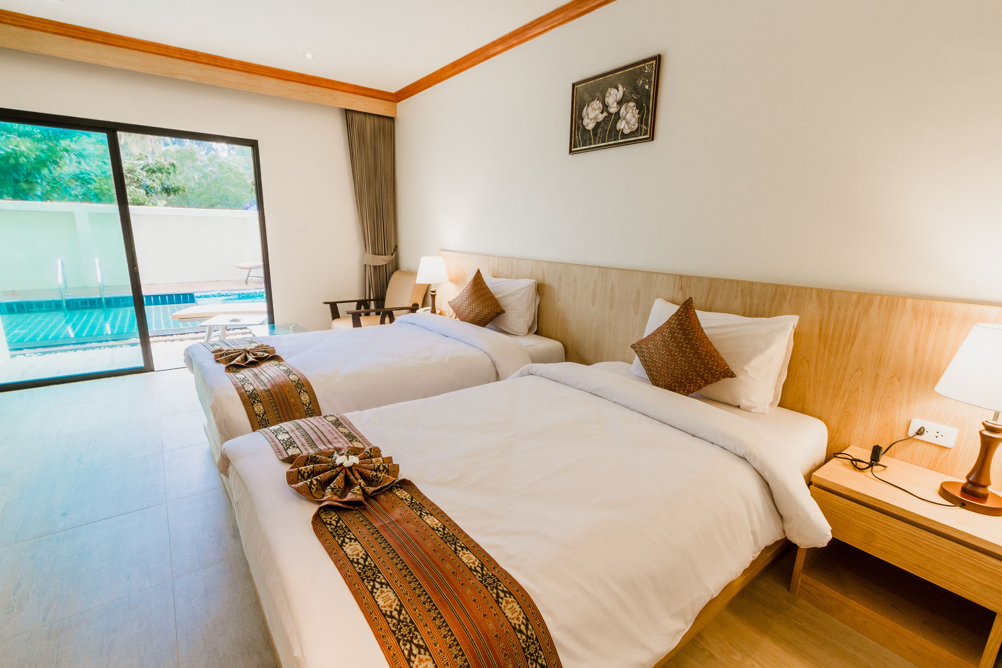 Une chambre d’hôtel avec deux lits, une grande porte-fenêtre coulissante donnant sur une piscine et une tête de lit en bois.