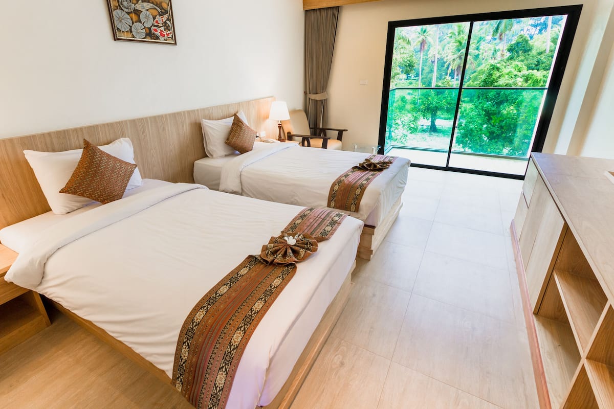 Une chambre d’hôtel avec deux lits, un bureau, une chaise et une grande fenêtre donnant sur un paysage verdoyant.