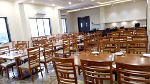 Un amplio comedor con varias mesas y sillas de madera, unidades de aire acondicionado en las paredes y una zona de cocina al fondo.