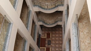 Un interior de varios niveles con suelo de mármol, barandillas de metal y una escalera central.