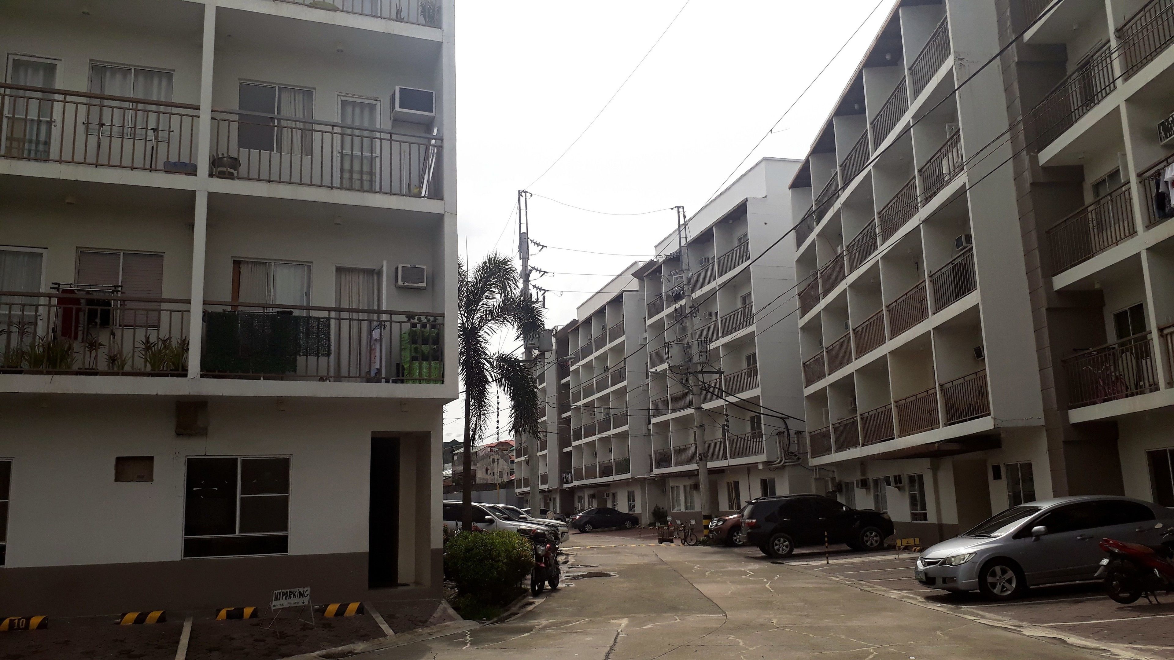 Un edificio residencial de varios pisos con balcones, coches estacionados y un cielo despejado.
