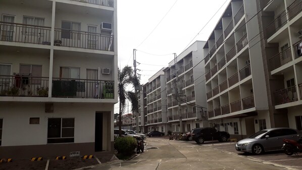 Un edificio residencial de varios pisos con balcones, coches estacionados y un cielo despejado.