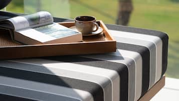 Un sofá moderno con una bandeja que sostiene un libro y una taza, ubicado cerca de una ventana con vistas a zonas verdes.