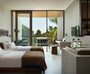 A modern hotel room with two beds, a desk, and a large window offering a view of palm trees and a building. - Dialoog Banyuwangi (Banyuwangi)