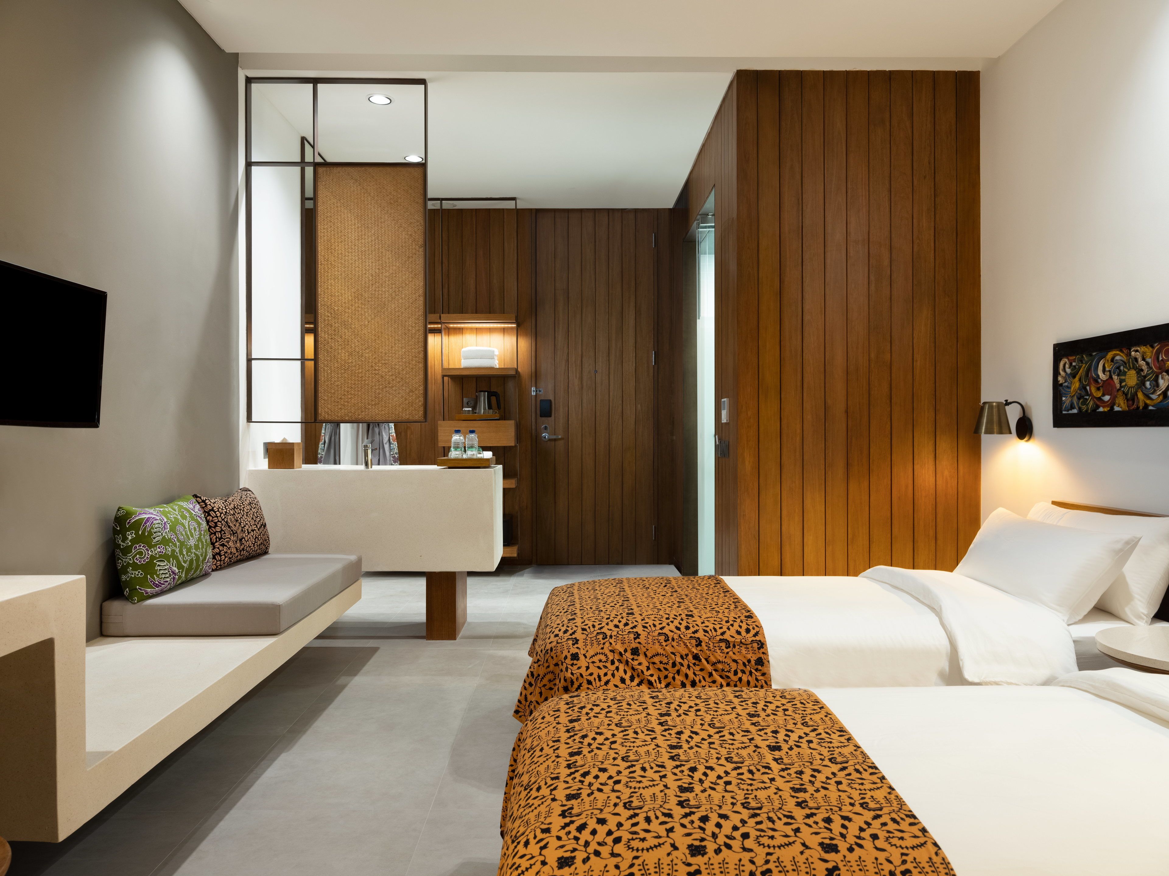 Quarto de hotel moderno com sofá, duas camas, uma kitchenette pequena e um espelho grande.