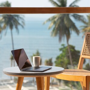 A laptop on a round table with a cup beside it, overlooking a beach with palm trees and the ocean. - Dialoog Banyuwangi (Banyuwangi)