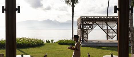 Un espacio tranquilo al aire libre con vistas al mar y a las montañas, que cuenta con una palmera y un porche de madera.