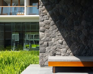 A modern outdoor seating area with a stone wall, a bench, and a glass railing overlooking a grassy area. - Dialoog Banyuwangi (Banyuwangi)