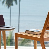 Uma cadeira de madeira com assento trançado e um laptop sobre uma mesinha redonda.
