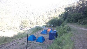 Un camping con varias tiendas de campaña, un sendero de tierra y un paisaje colinas.