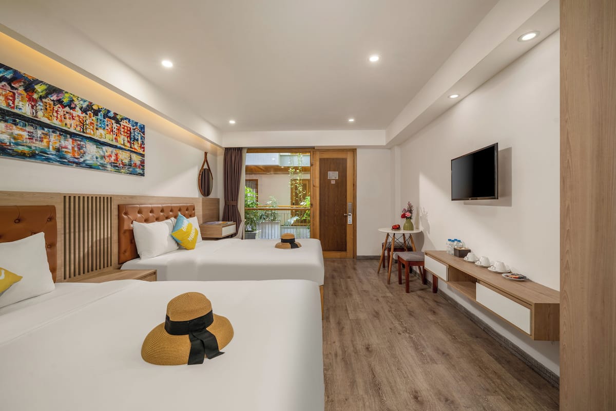 A hotel room with two beds, a TV, a desk, and a painting on the wall.