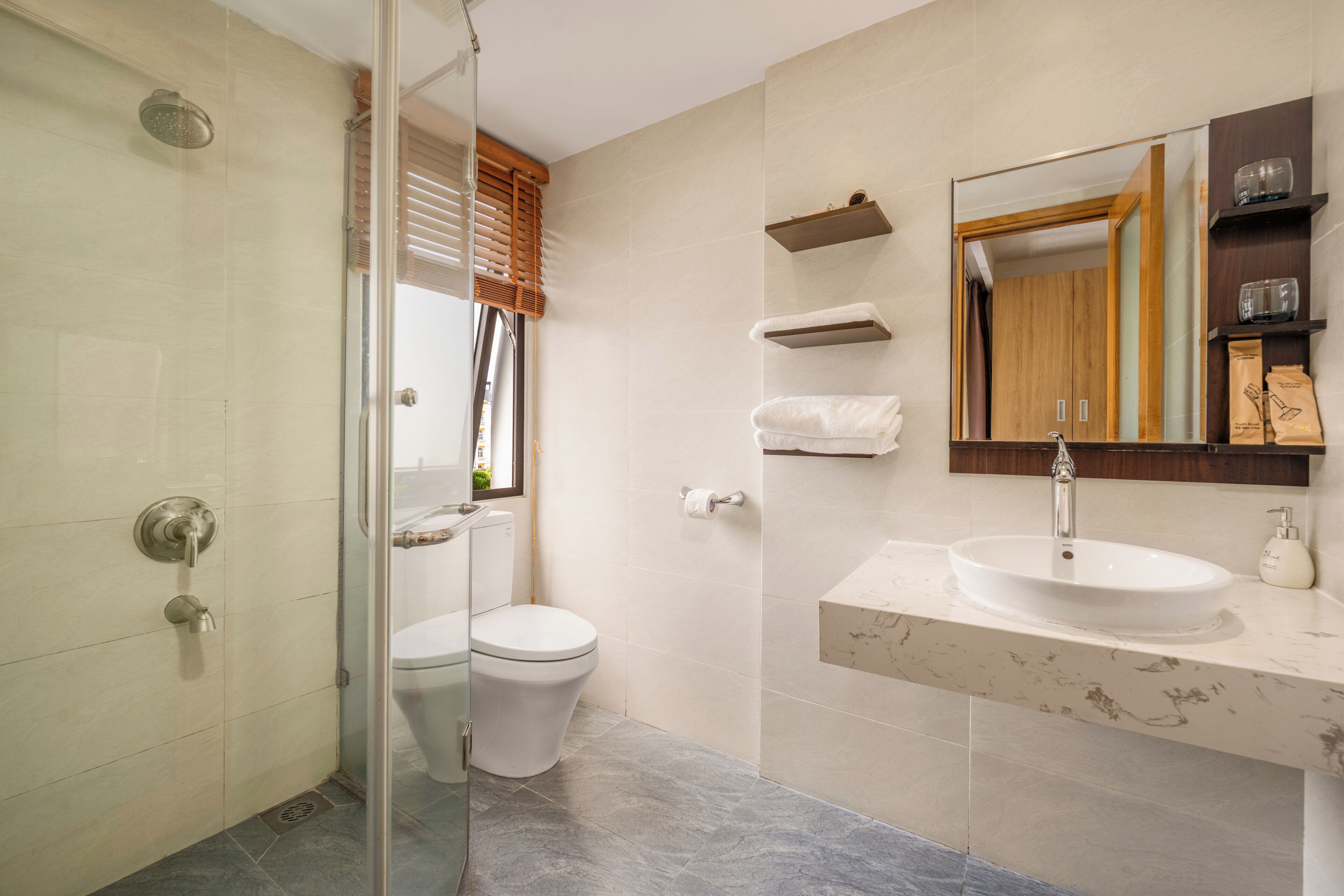 A modern bathroom with a glass-enclosed shower, a toilet, a sink with a marble countertop, and a mirror with a wooden frame.